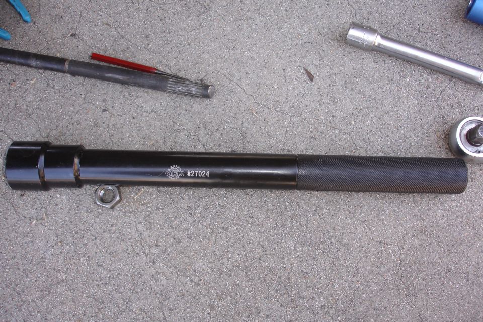 black tool with knurled handle and a nut next to it, some other tools in background