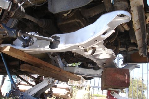 1992 Ford Taurus - Underside view of a car's subframe assembly being worked on, supported by mechanical jacks and wooden blocks.