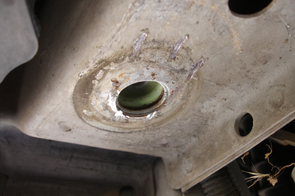 Close-up of a corroded metal subframe part with a green bushing and weld marks