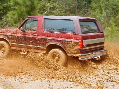 1990 Ford Bronco - A red 1990 Ford Bronco navigates a muddy trail, kicking up dirt as it goes.