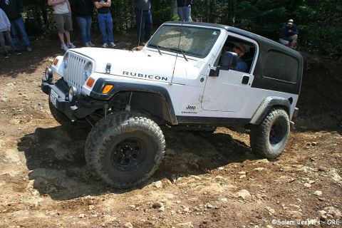 2005 Jeep Wrangler - A white Jeep Wrangler Rubicon navigates a challenging off-road course with onlookers in the background.