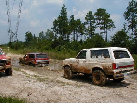 1990 Ford Bronco - A white 1990 Ford Bronco is being towed from a muddy area by another vehicle.