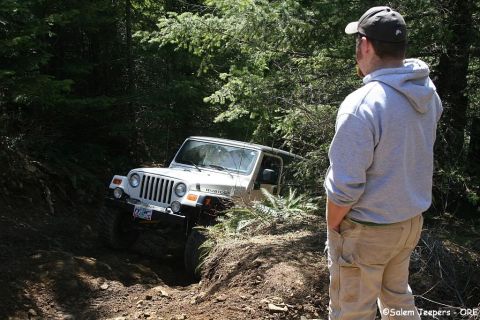 2005 Jeep Wrangler - A Jeep Wrangler is shown on a challenging off-road trail, with a person observing from the side.