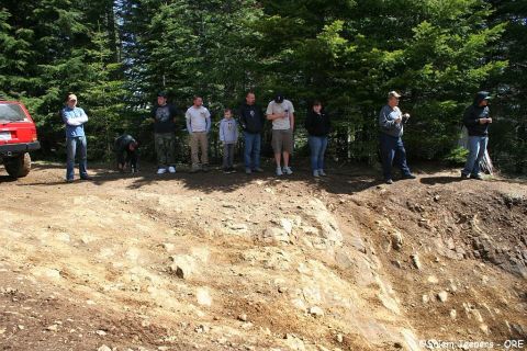 2005 Jeep Wrangler - A group of people stand by trees on a dirt road, with a red SUV parked to the left.
