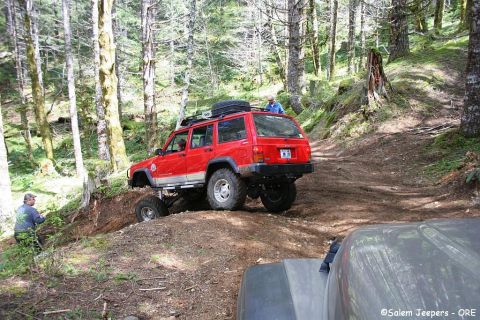 2005 Jeep Wrangler - Red Jeep Cherokee XJ climbs a steep, wooded trail with another vehicle close behind.