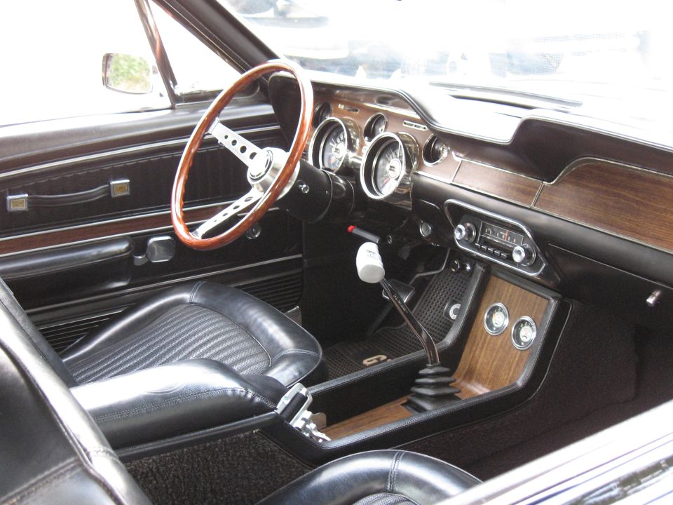 Black 1960s Mustang interior with wood-rim steering wheel, woodgrain dash and manual shifter