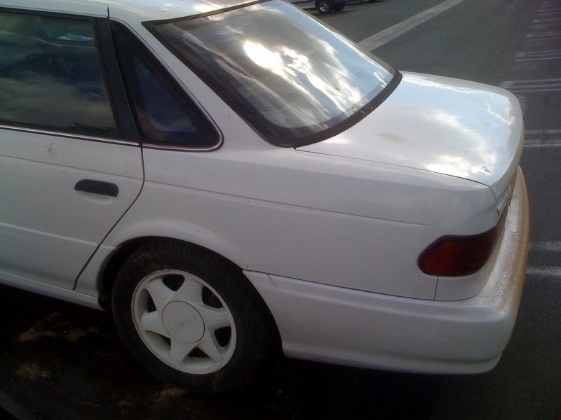 Rear quarter of a white 1990s Ford Taurus sedan in a parking lot
