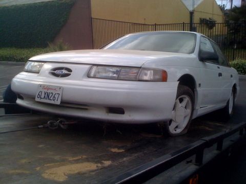 1992 Ford Taurus - Front view of a white 1992 Ford Taurus being towed, showing its California license plate.