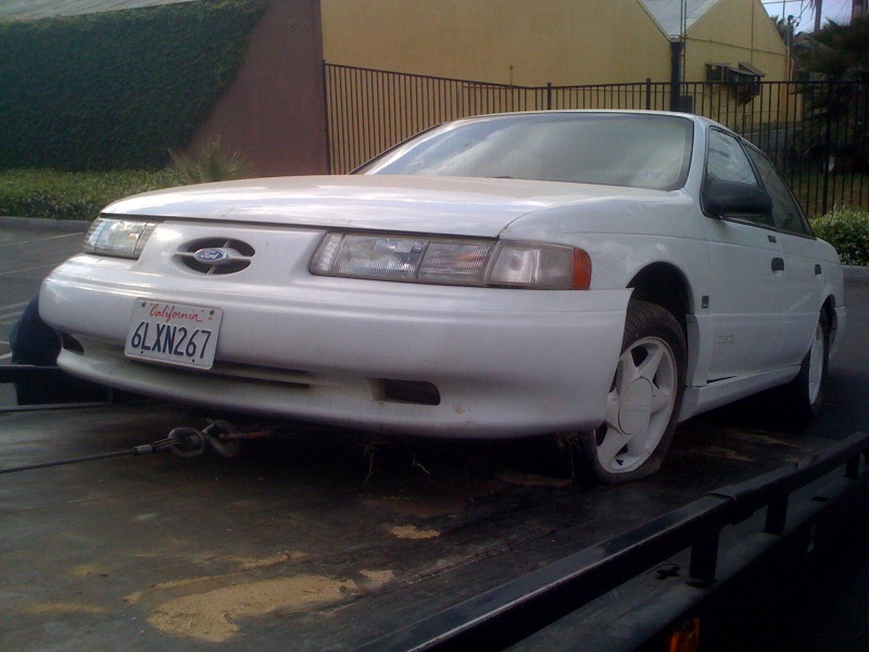 1992 Ford Taurus with a flat tire on a tow truck, California license plate 6LXN267