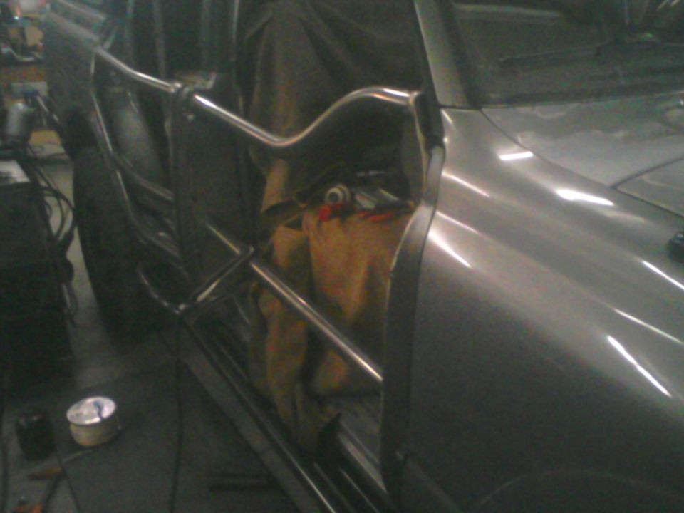 Close view of a shop-built tube door on a gray truck in a garage with welder behind