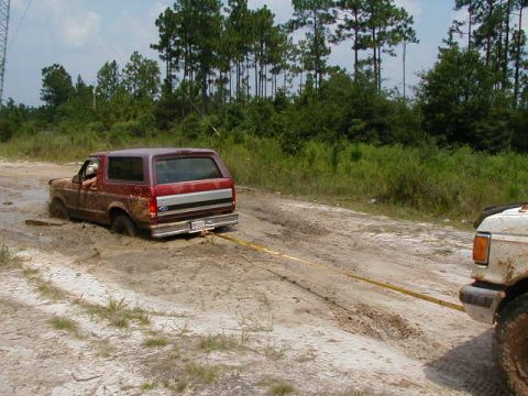 1990 Ford Bronco - A red Ford Bronco is stuck in the mud while another vehicle attempts to pull it out with a yellow tow strap.