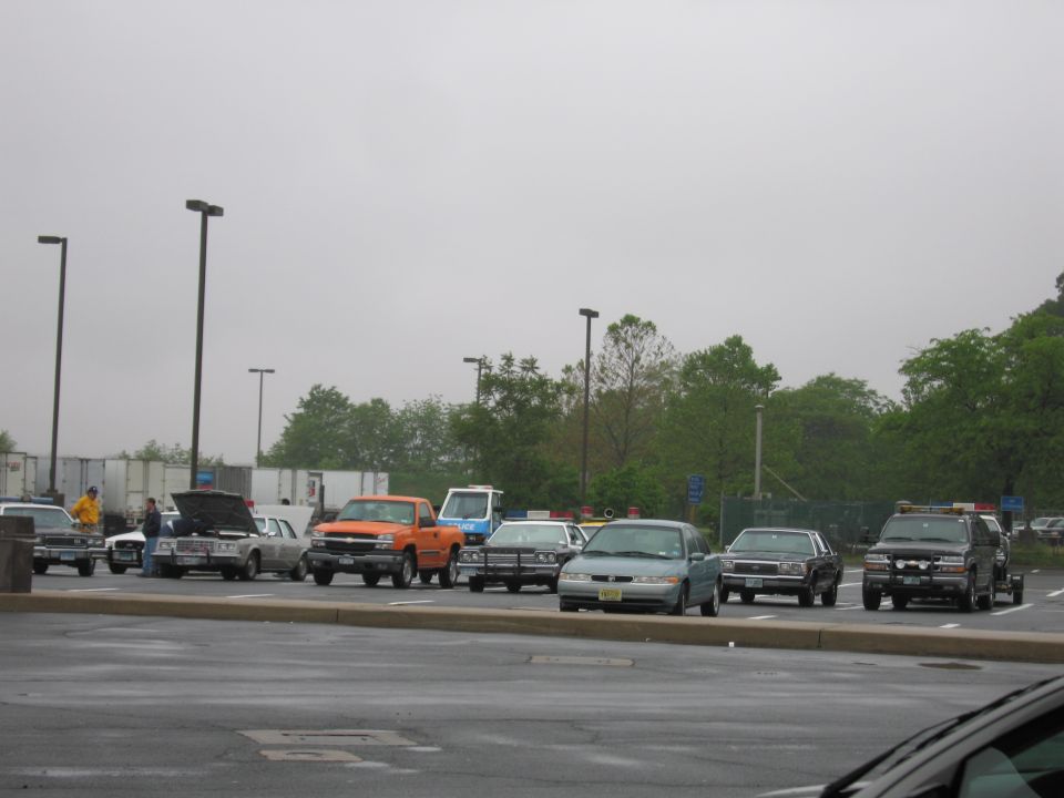 Row of vintage cars and pickups in a wet parking lot under gray sky