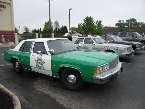 1991 Ford Crown Victoria - Several police cars are parked in a lot, including a green and white Sheriff's vehicle.