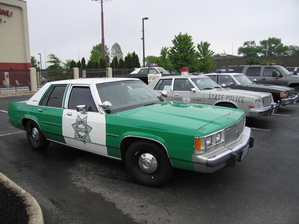 Green and white sheriff sedan parked beside other police cruisers