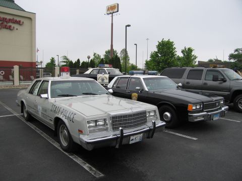 1991 Ford Crown Victoria - Several police vehicles are parked in a lot, including a silver sedan with "STATE POLICE" markings.