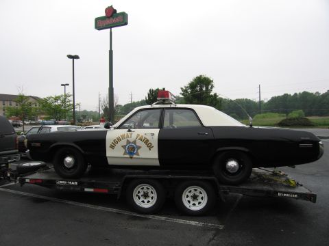 1991 Ford Crown Victoria - A black and white highway patrol car is parked on a trailer under a cloudy sky.