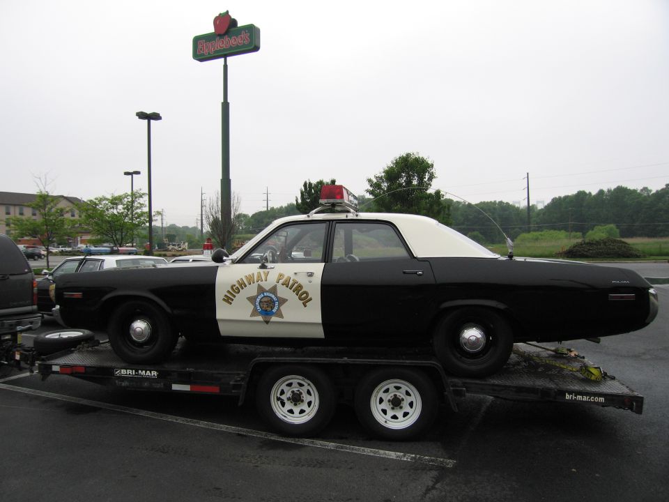 Black-and-white Highway Patrol sedan on a trailer near an Applebee's sign