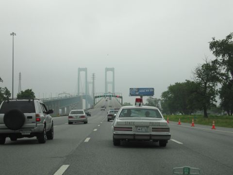 1991 Ford Crown Victoria - A state police car is seen on the highway approaching a large suspension bridge on a cloudy day.