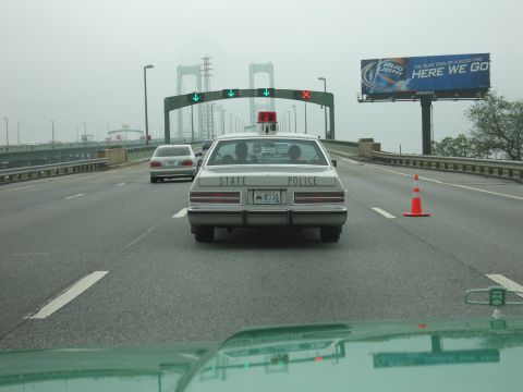 1991 Ford Crown Victoria - A 1991 Ford Crown Victoria police car is seen from behind on a highway, with other vehicles and a billboard in the background.