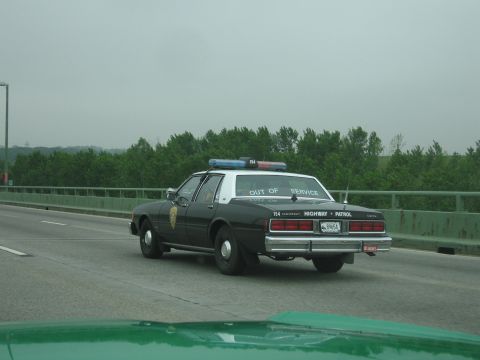 1991 Ford Crown Victoria - A highway patrol car is seen driving on a bridge with trees in the background.