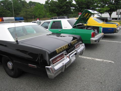 1991 Ford Crown Victoria - Several vintage patrol cars are lined up, with the black Dodge in the foreground showing 'HIGHWAY PATROL' on its rear.