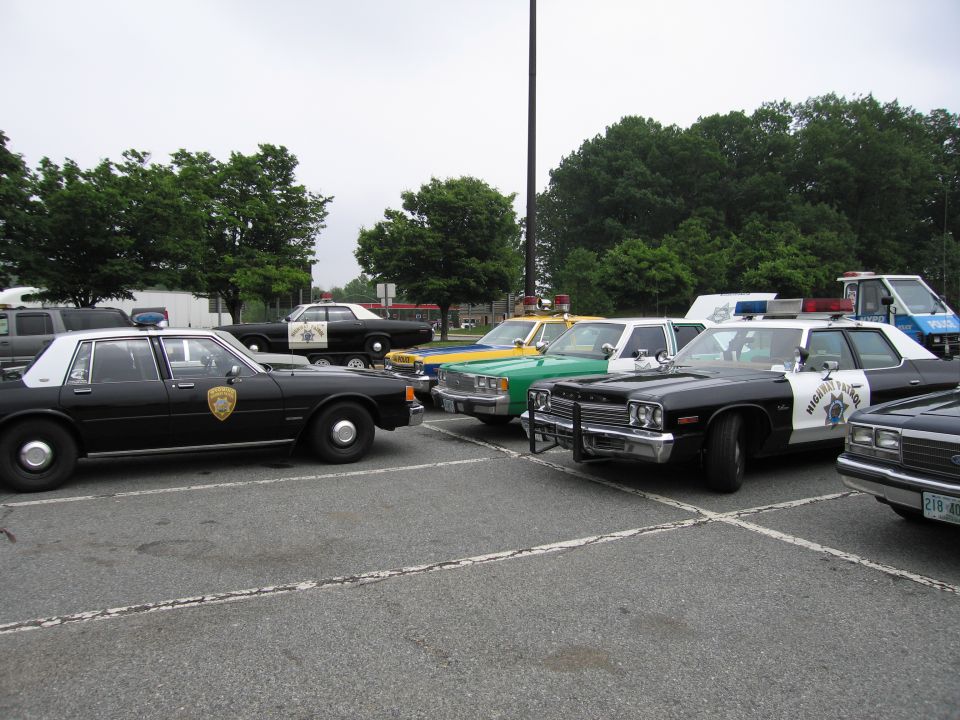 Several vintage police cars in black, green, and yellow parked in a paved lot