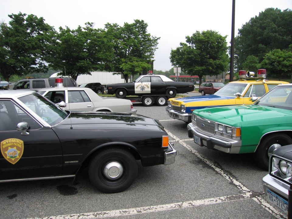 Black Wyoming sheriff sedan in foreground with green and yellow police cars and a trailered patrol car