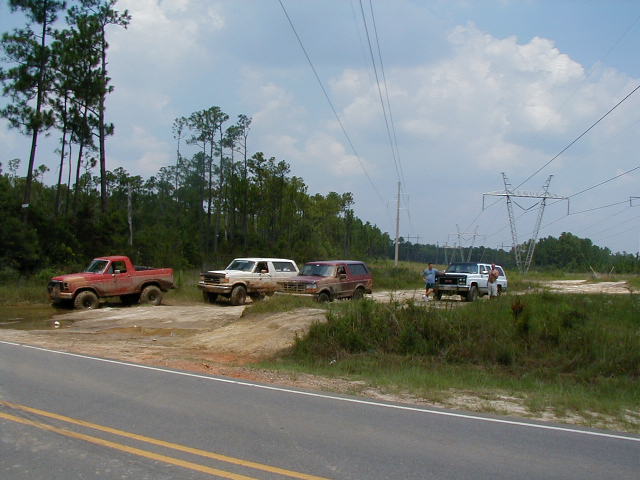 Four-wheel drive vehicles in a muddy area with power lines overhead