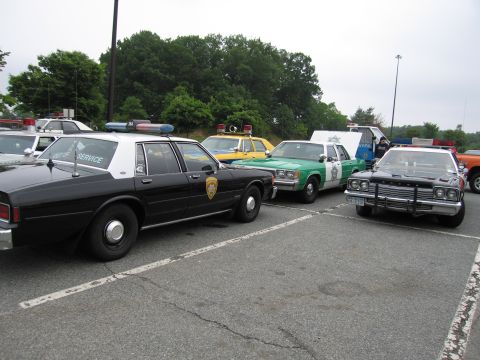 1991 Ford Crown Victoria - A collection of marked police vehicles are parked in an outdoor lot under an overcast sky.