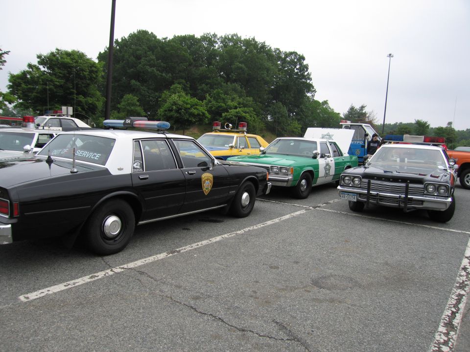 Black-and-white police sedan beside green-and-white and other vintage patrol cars in a lot