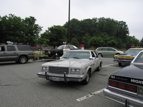 1991 Ford Crown Victoria - Several police vehicles are parked in a lot under an overcast sky.