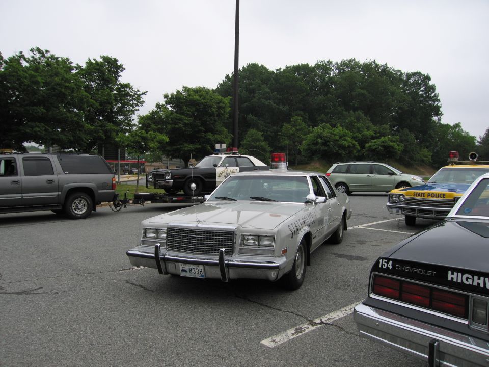 Silver Chrysler police sedan parked among yellow State Police and black Highway Patrol cars