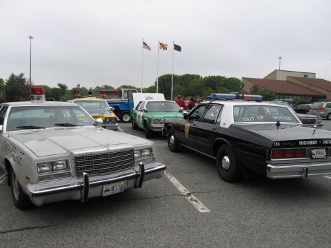 1991 Ford Crown Victoria - Several police vehicles are parked together, including a silver car with "STATE POLICE" on the door and a black and white car marked "HIGHW…