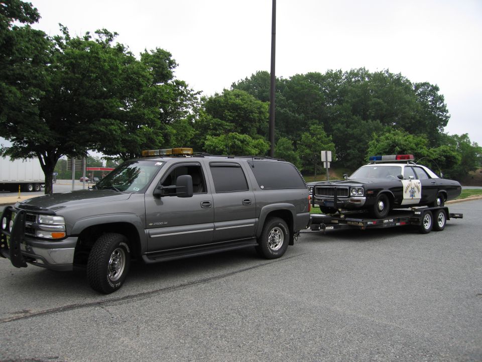Gray Chevrolet Suburban towing a trailer carrying a black-and-white Highway Patrol cruiser
