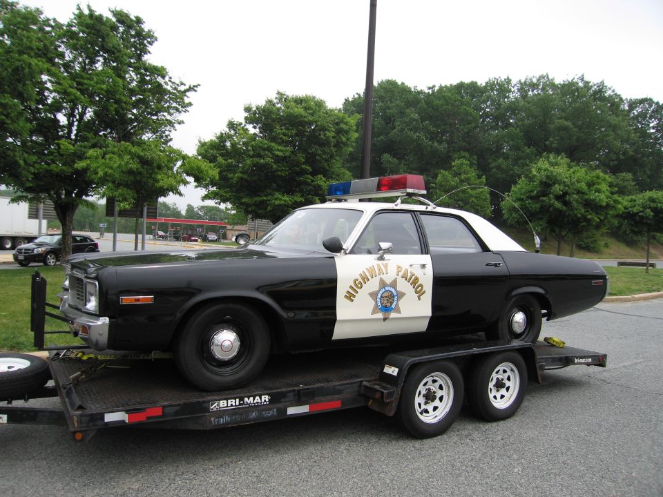 Black-and-white Highway Patrol sedan with gold star emblem loaded on a dual-axle trailer