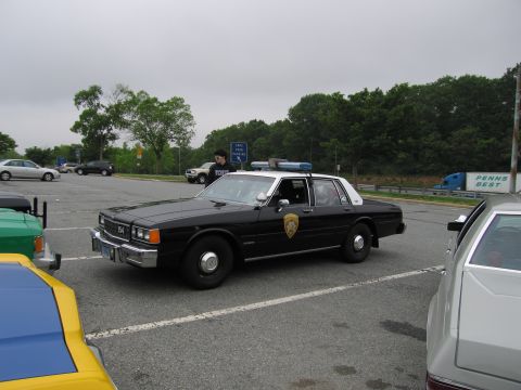 1991 Ford Crown Victoria - A police car with lights on top is parked in a lot with other vehicles visible.