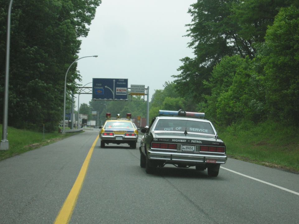 Two vintage police cars driving on a highway, black Highway Patrol Caprice marked OUT OF SERVICE in front