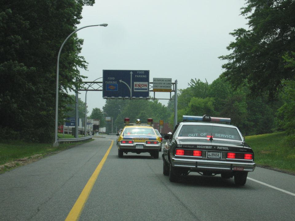 Black Highway Patrol Caprice and yellow patrol car driving under FOOD PARKING EXXON highway sign
