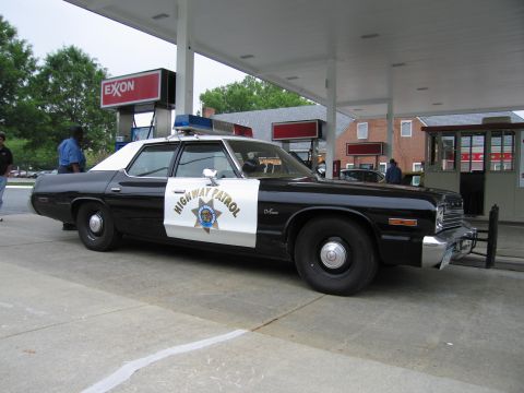 1991 Ford Crown Victoria - A vintage highway patrol car is parked under a gas station canopy, with an Exxon sign visible.