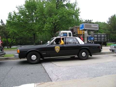 1991 Ford Crown Victoria - Police car at a gas station, with a person in the driver's seat.