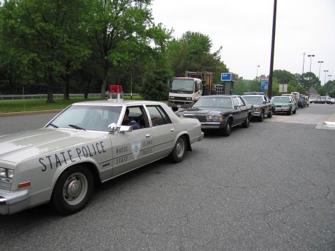 1991 Ford Crown Victoria - A line of police cars and other vehicles are parked on a paved surface.
