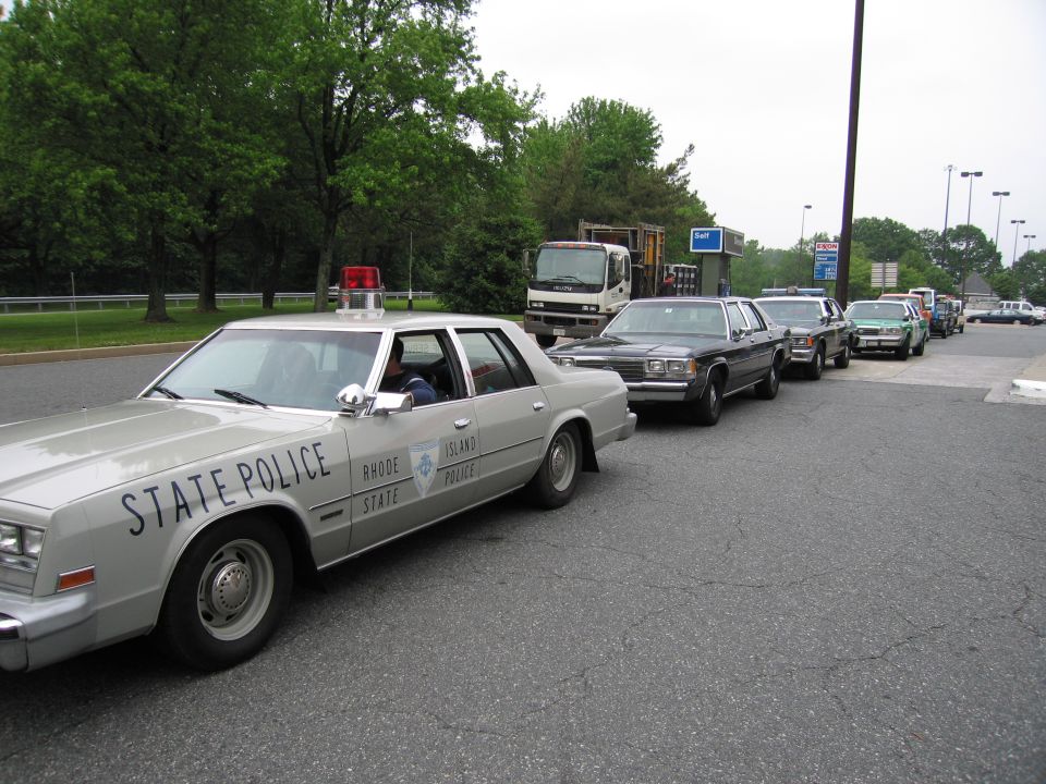 Silver Rhode Island State Police sedan leading a line of vehicles in a parking lot