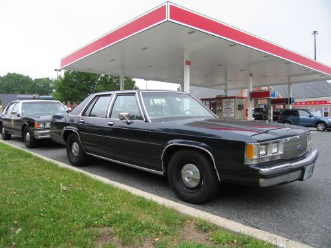 1991 Ford Crown Victoria - Two sedans are parked at a gas station under a red and white canopy.