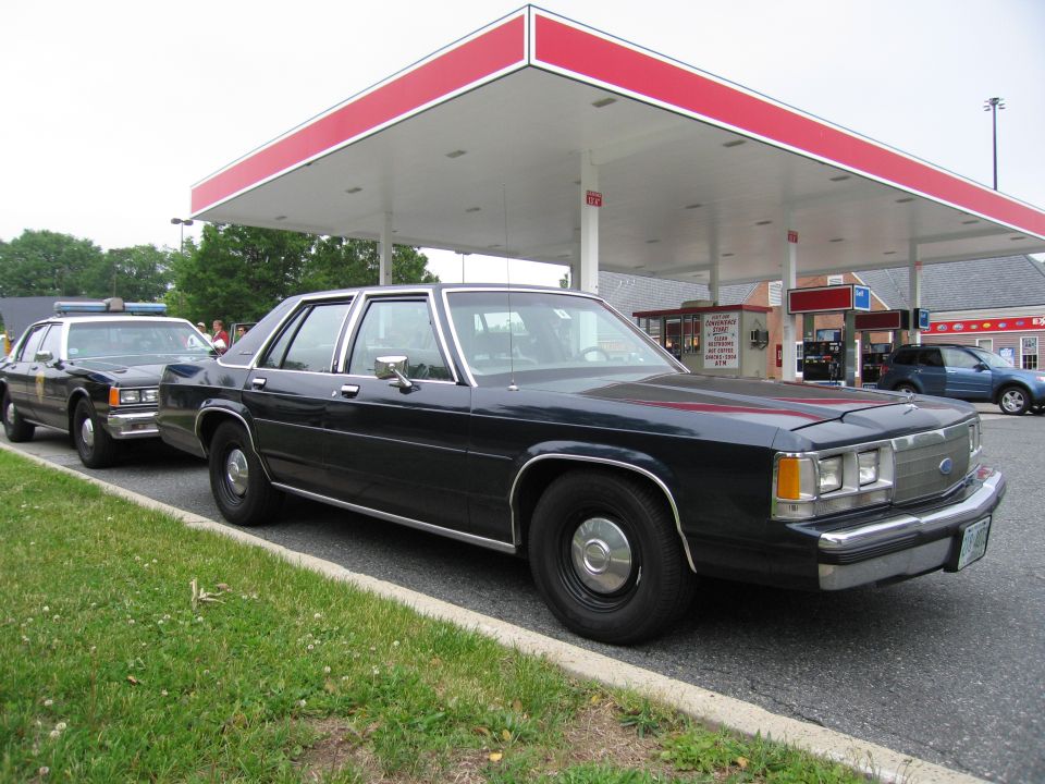 Black Ford four-door sedan at gas station, second black police car behind