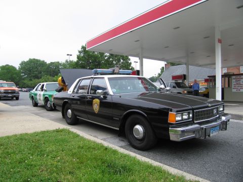 1991 Ford Crown Victoria - A black police car is parked at a gas station with its hood open.
