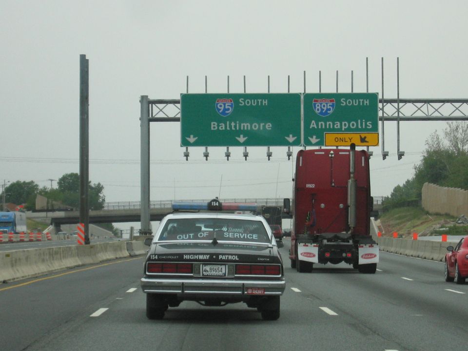 Police car and red semi on highway beneath I-95 and I-895 South overhead signs