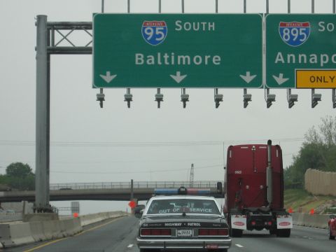 1991 Ford Crown Victoria - A police car and a semi-truck are on the highway under overhead signs for Baltimore and Annapolis.