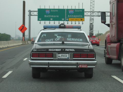 1991 Ford Crown Victoria - A Chevrolet Caprice police car, marked "HIGHWAY PATROL" and "OUT OF SERVICE", is seen on the highway.