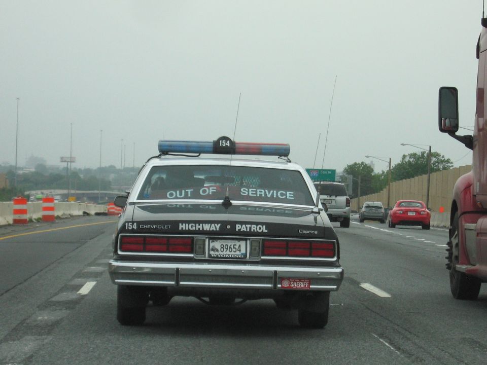Rear of black Highway Patrol Caprice on highway beside red semi