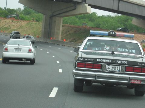 1991 Ford Crown Victoria - A Chevrolet Caprice police car, marked 'HIGHWAY PATROL' and 'OUT OF SERVICE', is seen on the highway.